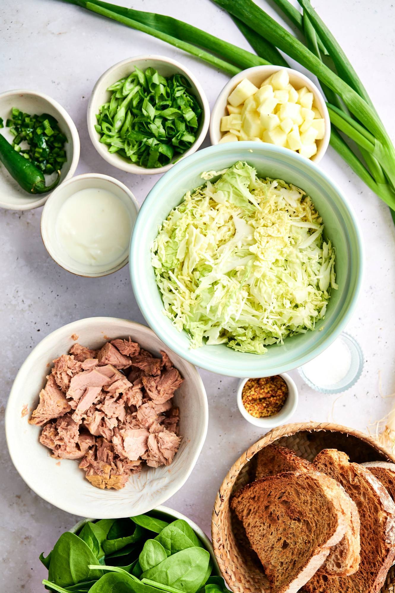 Ingredients for cabbage tuna salad including canned tuna, shredded green cabbage, Greek yogurt, mustard, green onions, and toasted bread.
