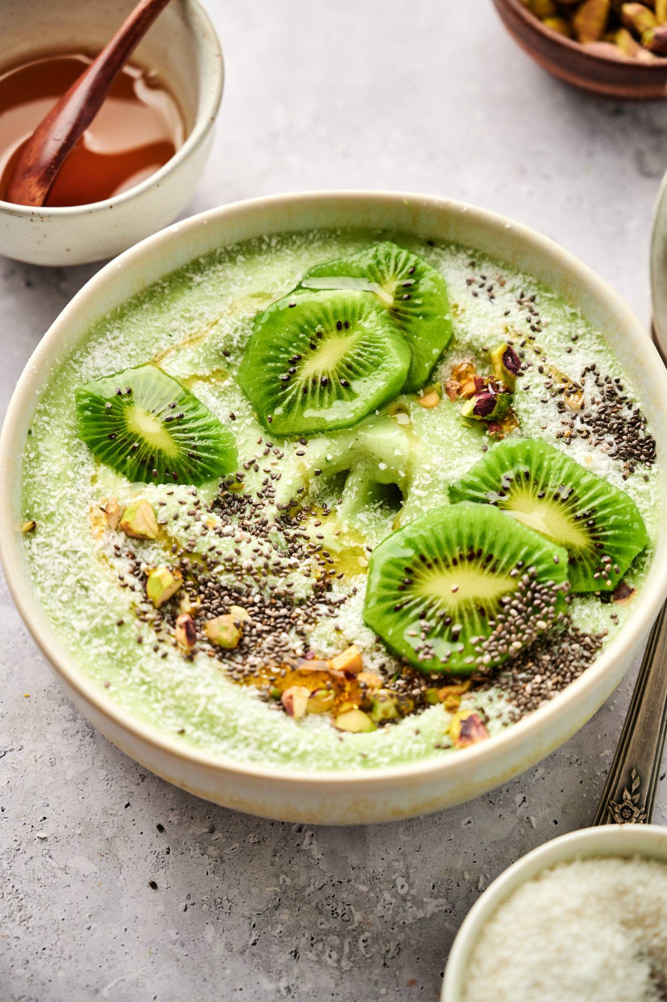 Spinach smoothie bowl with pineapple, mango, and banana topped with kiwi, chia seeds, and pistachios.
