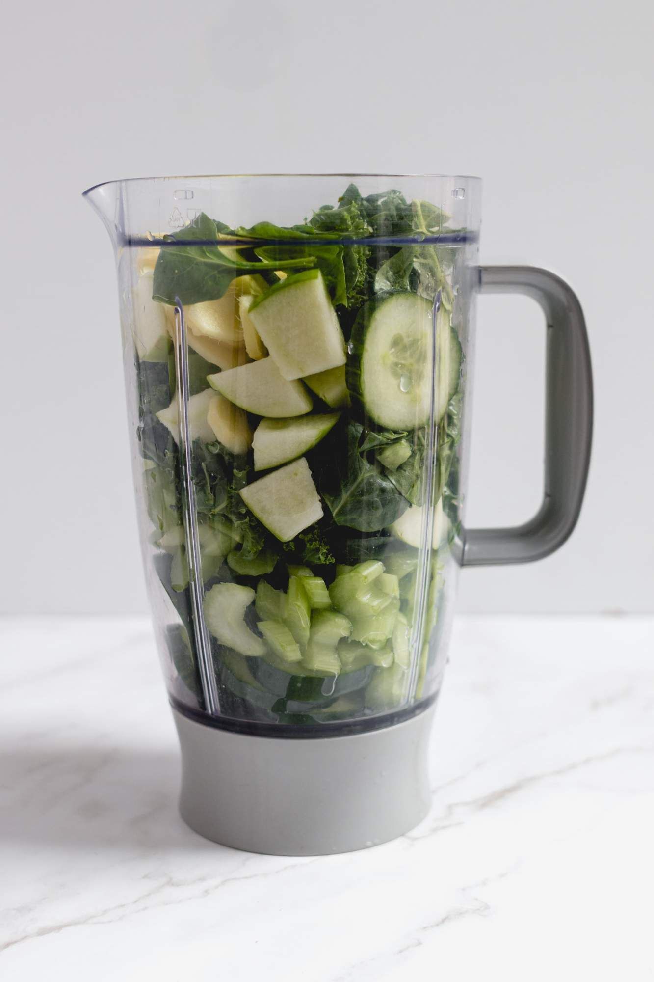 Blender filled with kale, spinach, celery, green apples, cucumbers, and lemon.