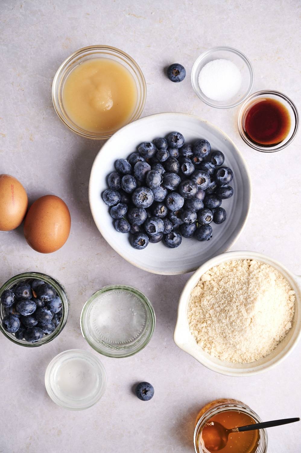 Ingredients for low carb almond pancakes including almond flour, blueberries, eggs, applesauce, water, vanilla extract, and coconut oil.