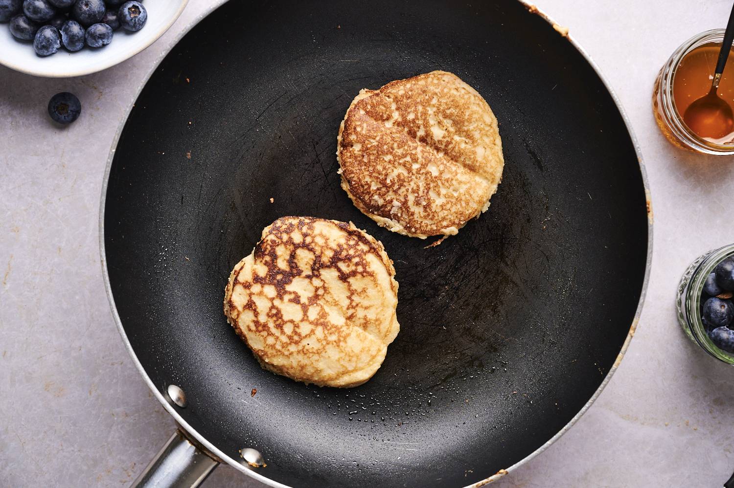 Almond flour pancakes cooking in a nonstick skillet with golden brown edges.