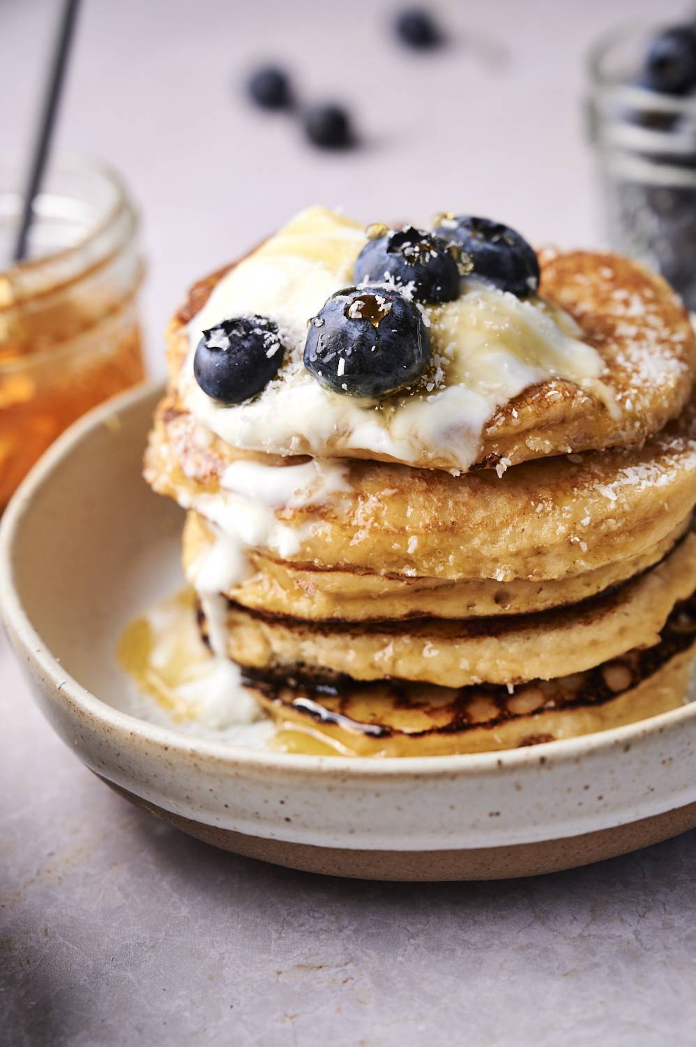 Stack of almond flour pancakes wit yogurt, blueberries, and maple syrup in a bowl.
