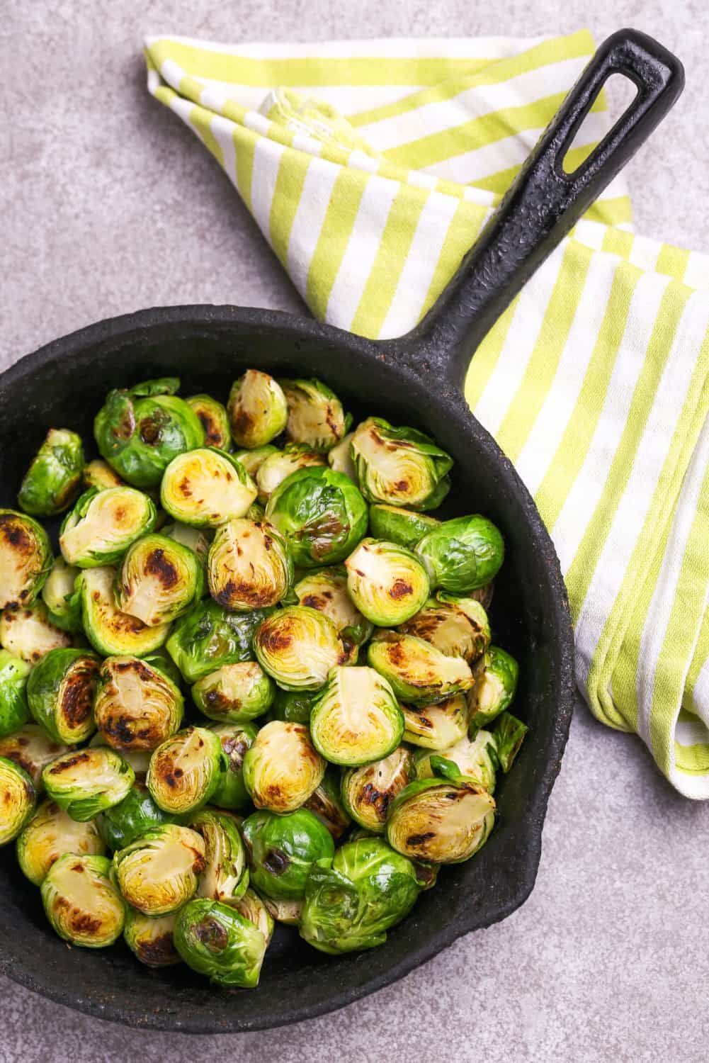 Easy roasted Brussels sprouts in a cast iron skillet with a yellow napkin.
