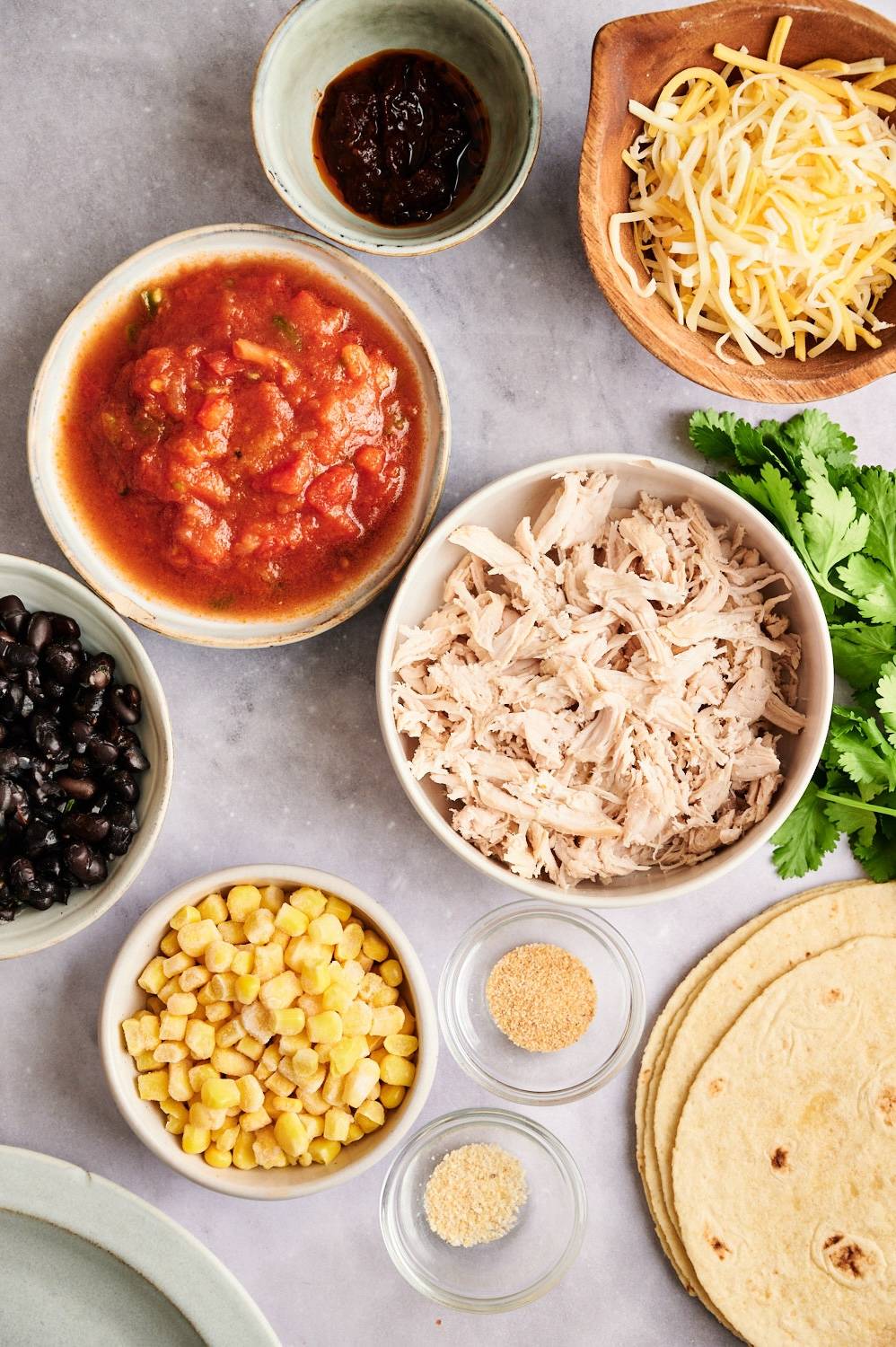 Ingredients for spicy chicken quesadillas including shredded chicken, corn, black beans, tortillas, cheese, salsa, and chipotle peppers.