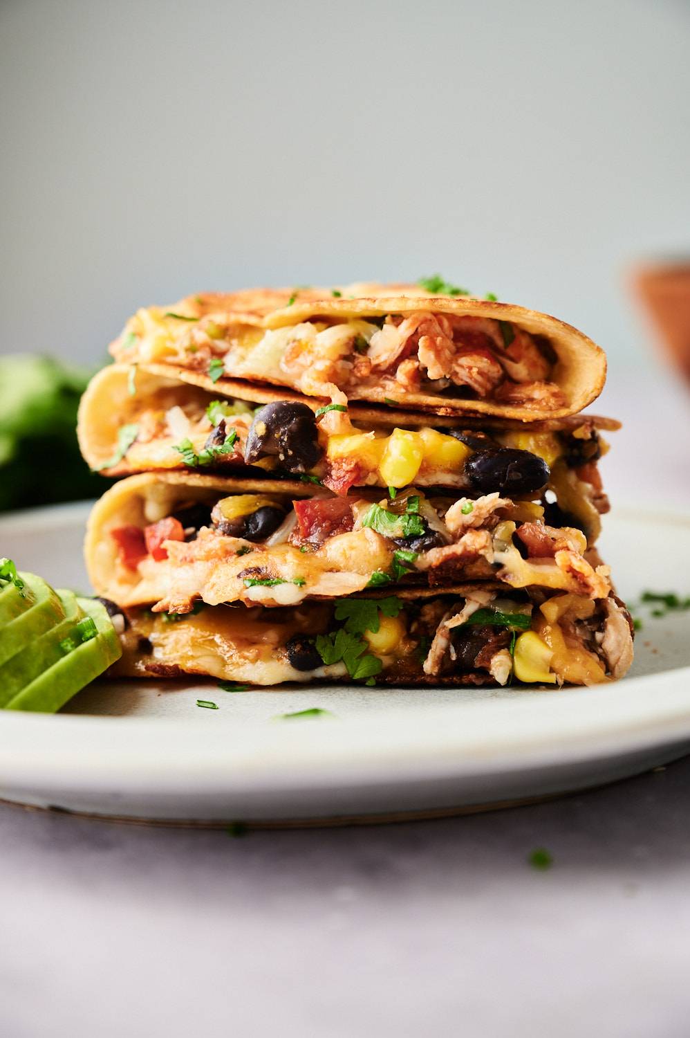 Chipotle chicken quesadillas with black beans and corn piled on a plate with avocado.