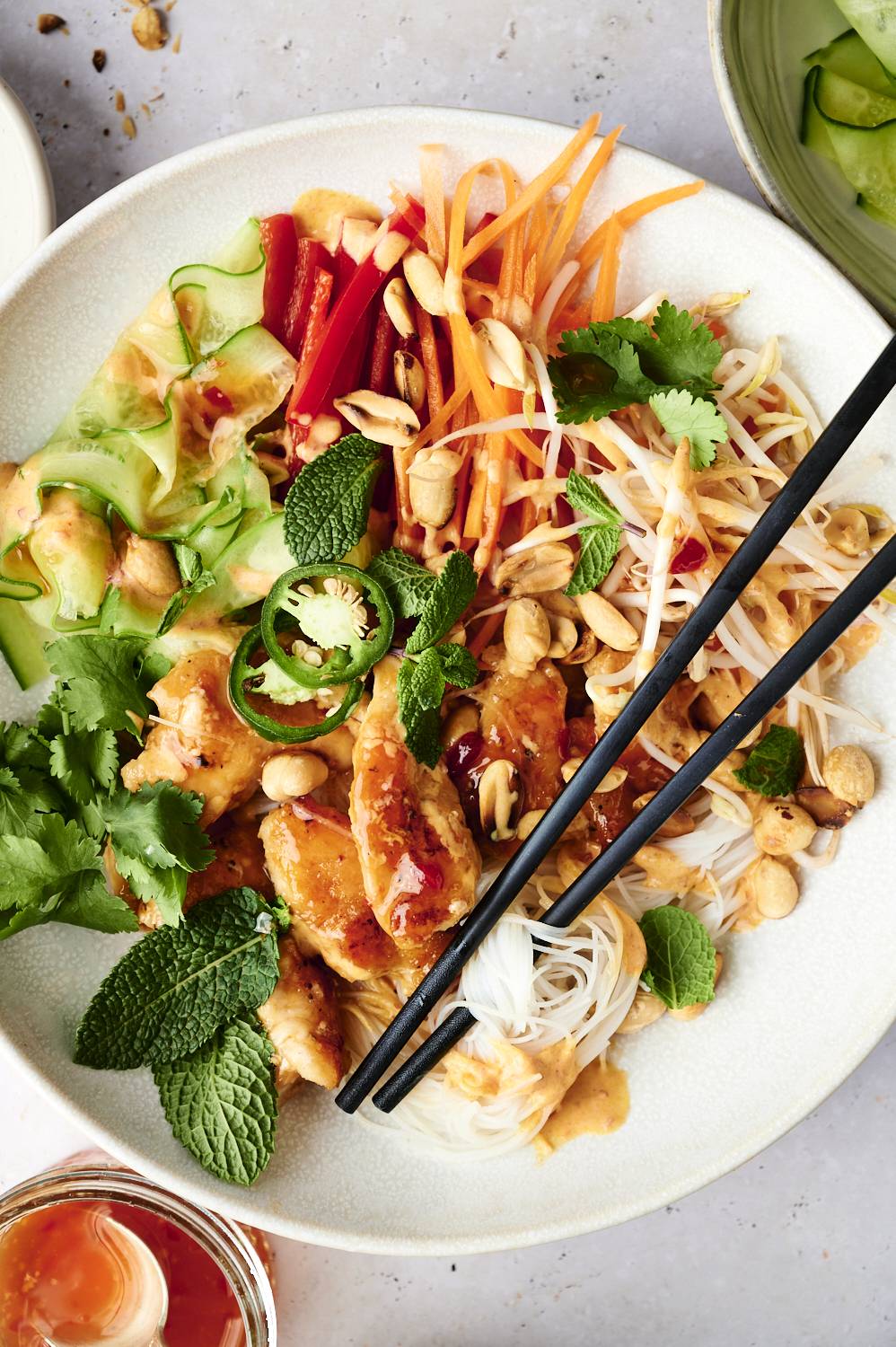 Vietnamese vermicelli noodle bowls with sweet chili chicken, noodles, vegetables, herbs, peanuts, and spicy sauce in bowl with chopsticks.
