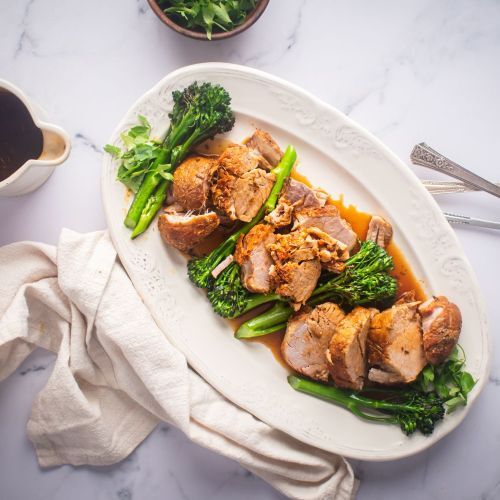 Slow cooker pork tenderloin with mustard sauce and broccolini on a white platter.
