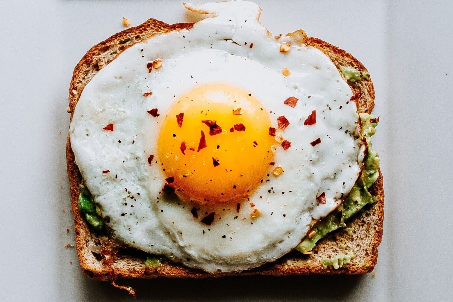 Eggs on a piece of toast with avocado and red pepper flakes.