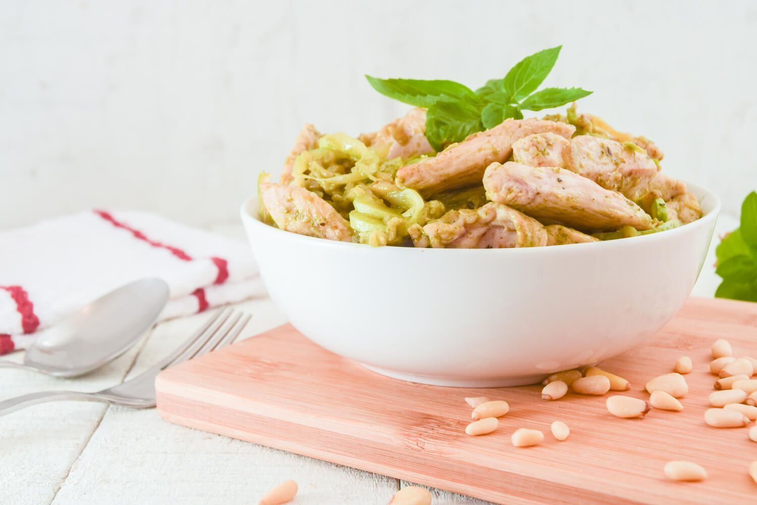 Pesto zoodles with chicken in a bowl with pine nuts on the side.
