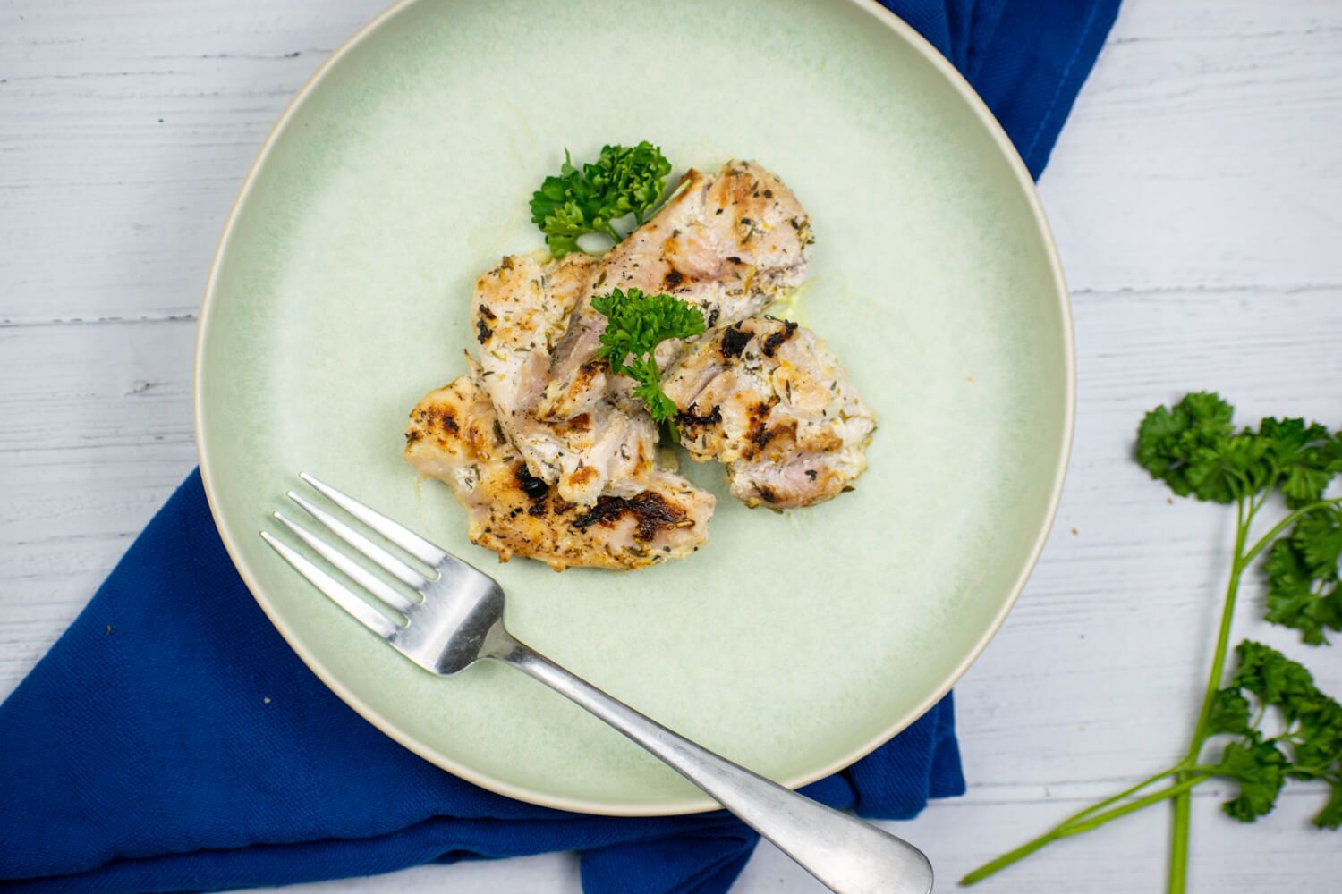 Greek chicken thighs with fresh parsley on a plate with a blue napkin.