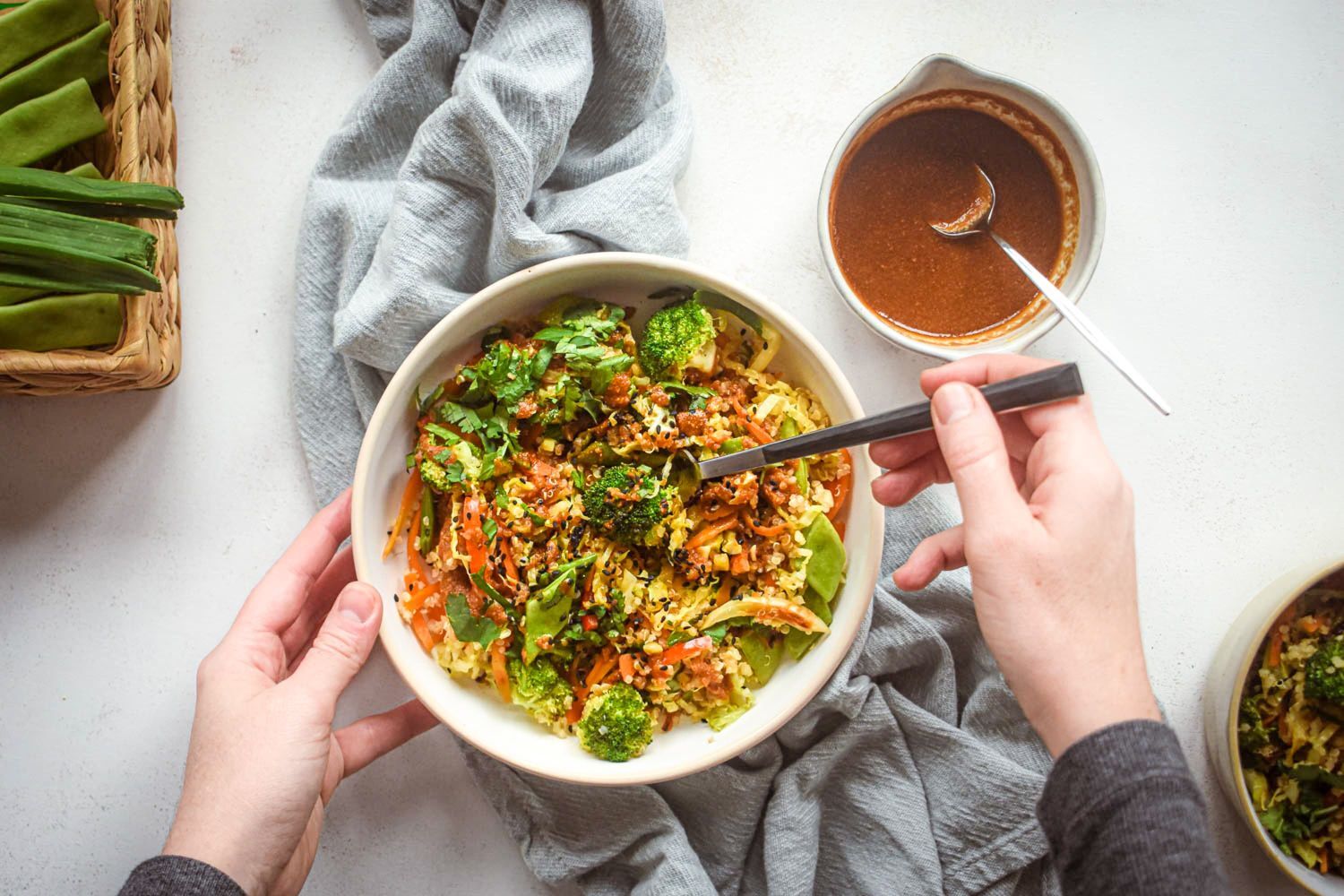 Asian quinoa stir fry with broccoli, carrots, cabbage, and snow peas in a bowl with stir fry sauce and sesame seeds.