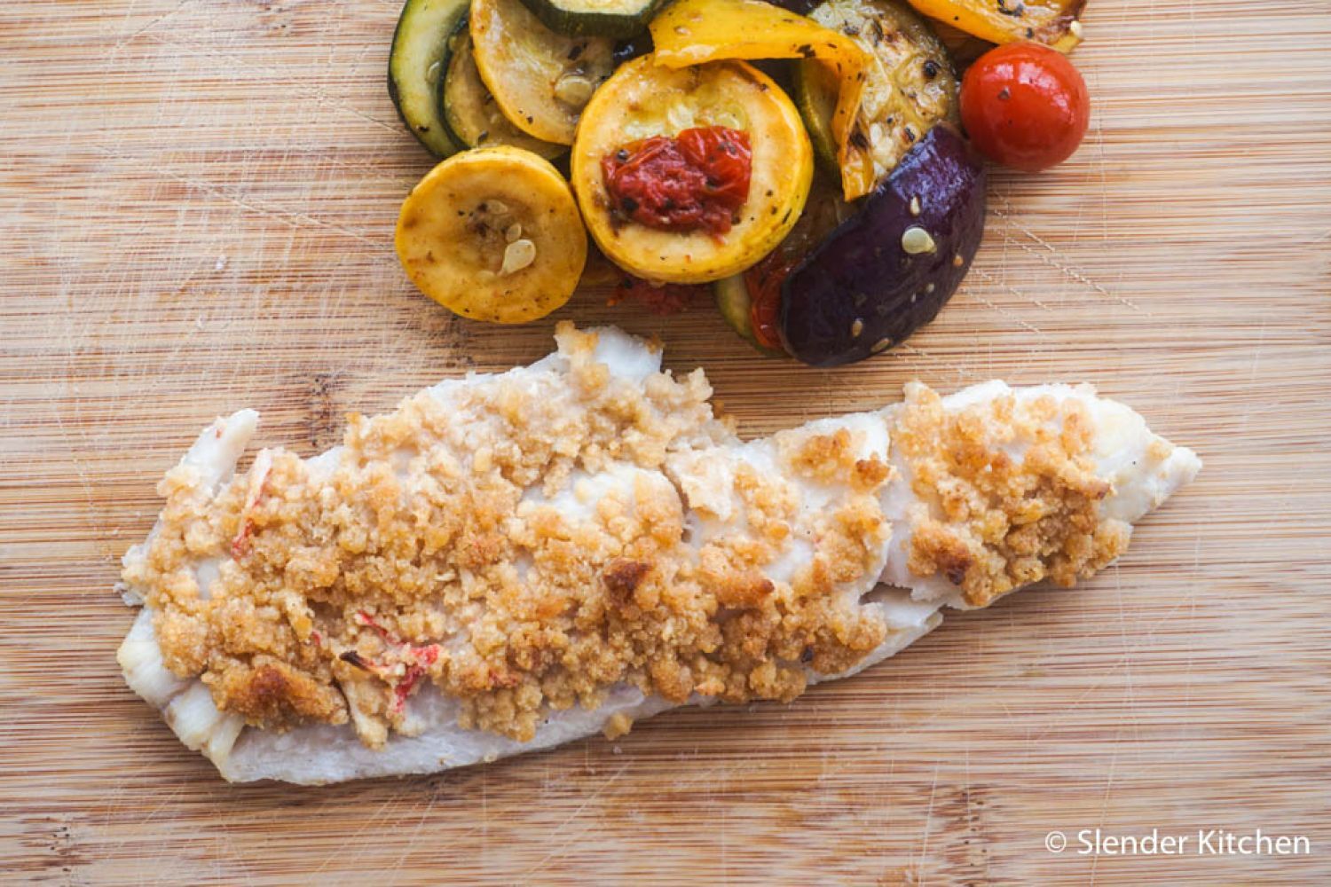 Baked haddock with seafood stuffing and vegetables on a cutting board.