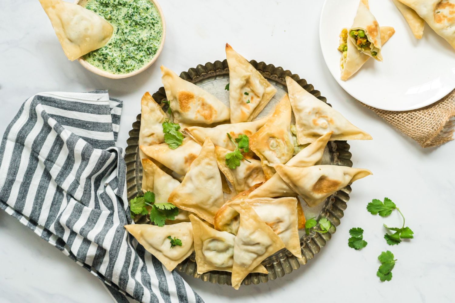 Baked samosa filled with potato, cauliflower, and peas on a plate with cilantro and mint dipping sauce.