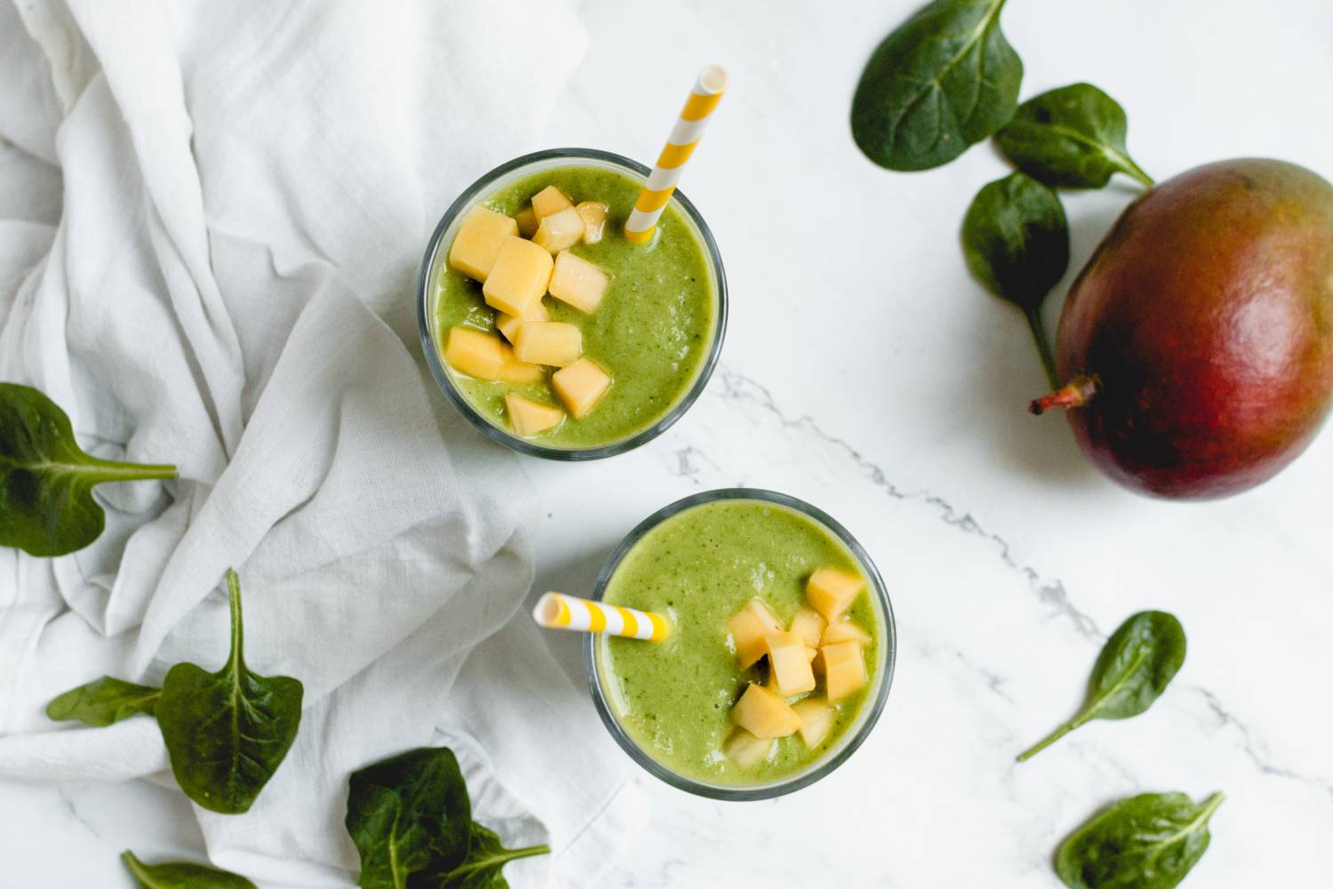 Green spinach and mango smoothie served in two glasses.