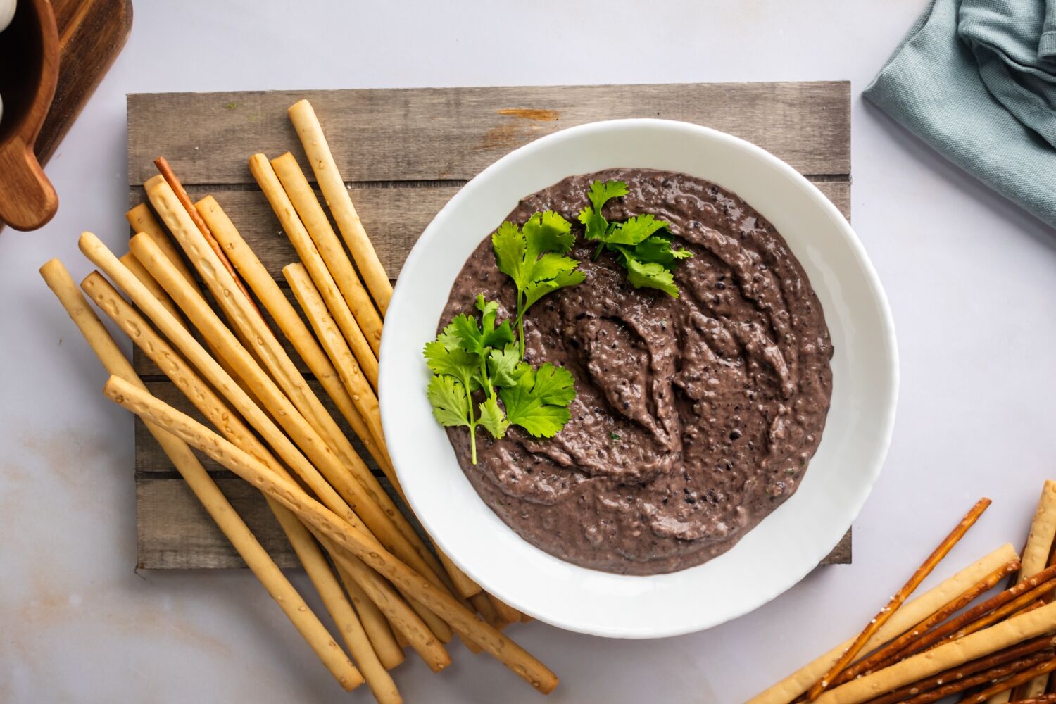 Black bean hummus in a bowl with cilantro with breadsticks and pretzels on the side.