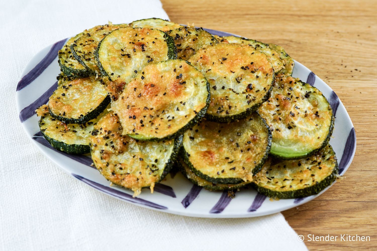 Black Pepper Parmesan zucchini chips with melted cheese and black pepper on thin slices of zucchini.