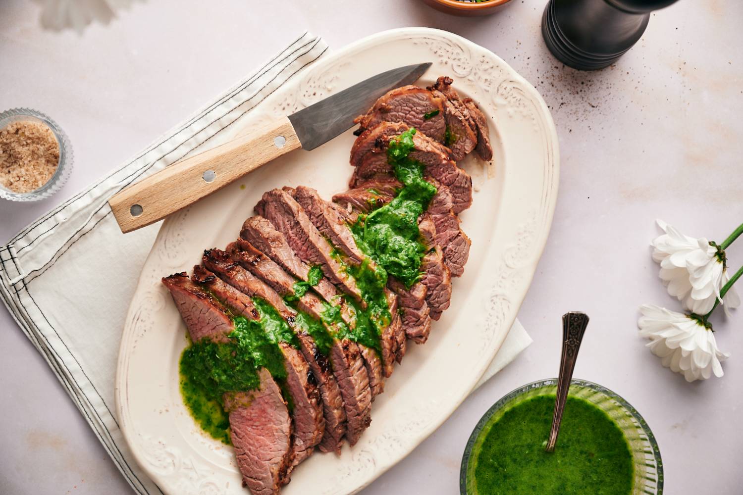 Broiled flank steak cooked until medium rare and sliced on a plate with chimichurri.