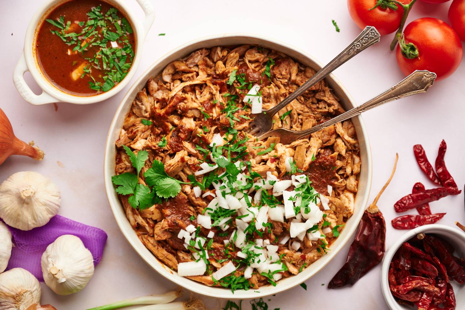 Chicken birria served in a bowl with shredded chicken in a red chile sauce with cilantro and onions.