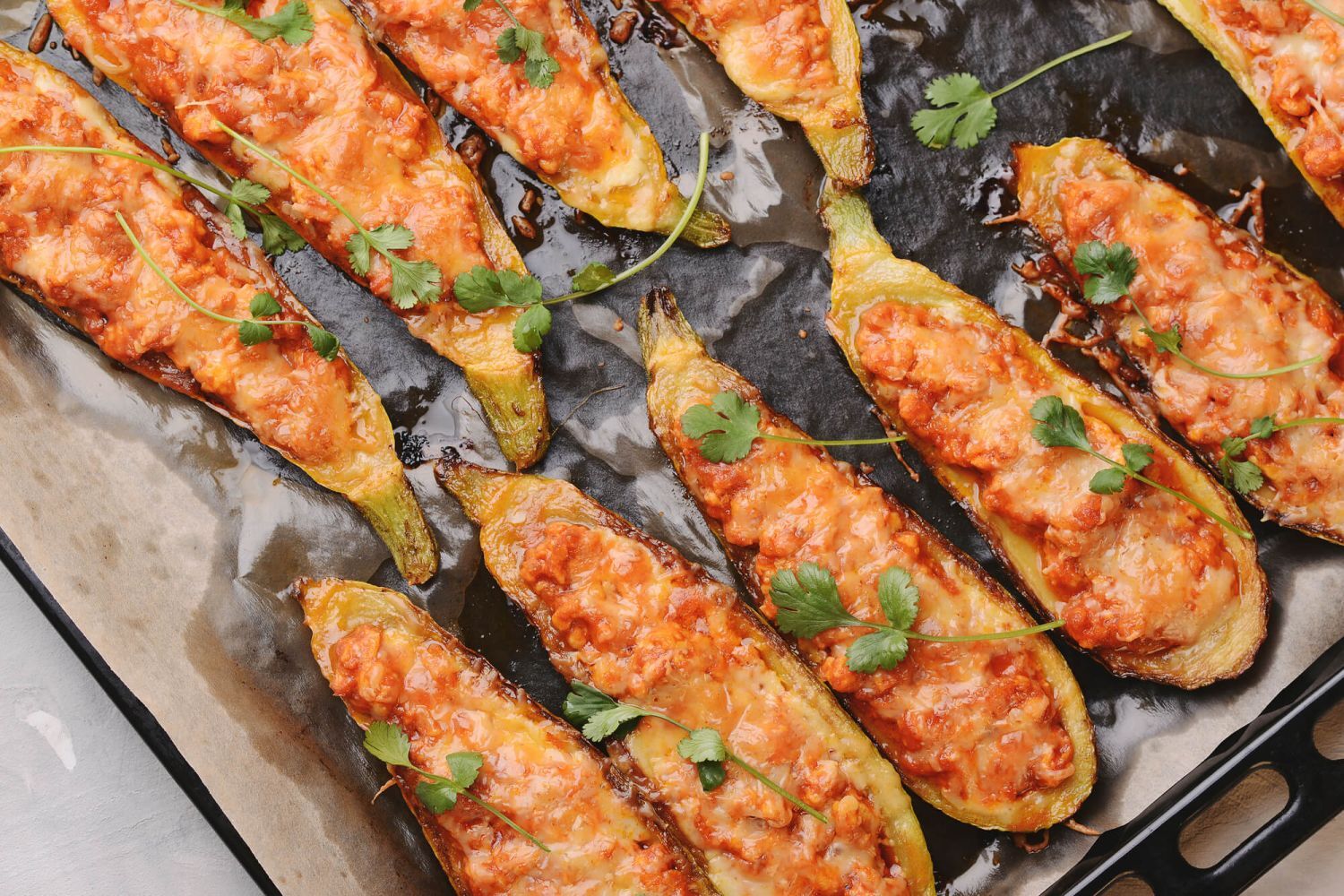 Chicken Parmesan zucchini boats with ground chicken, tomatoes, and melted cheese on a baking sheet.