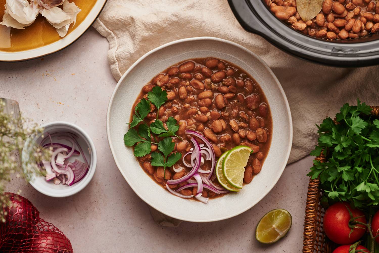 Crockpot pinto beans in a bowl with red onions, cilantro, and lime slices. 