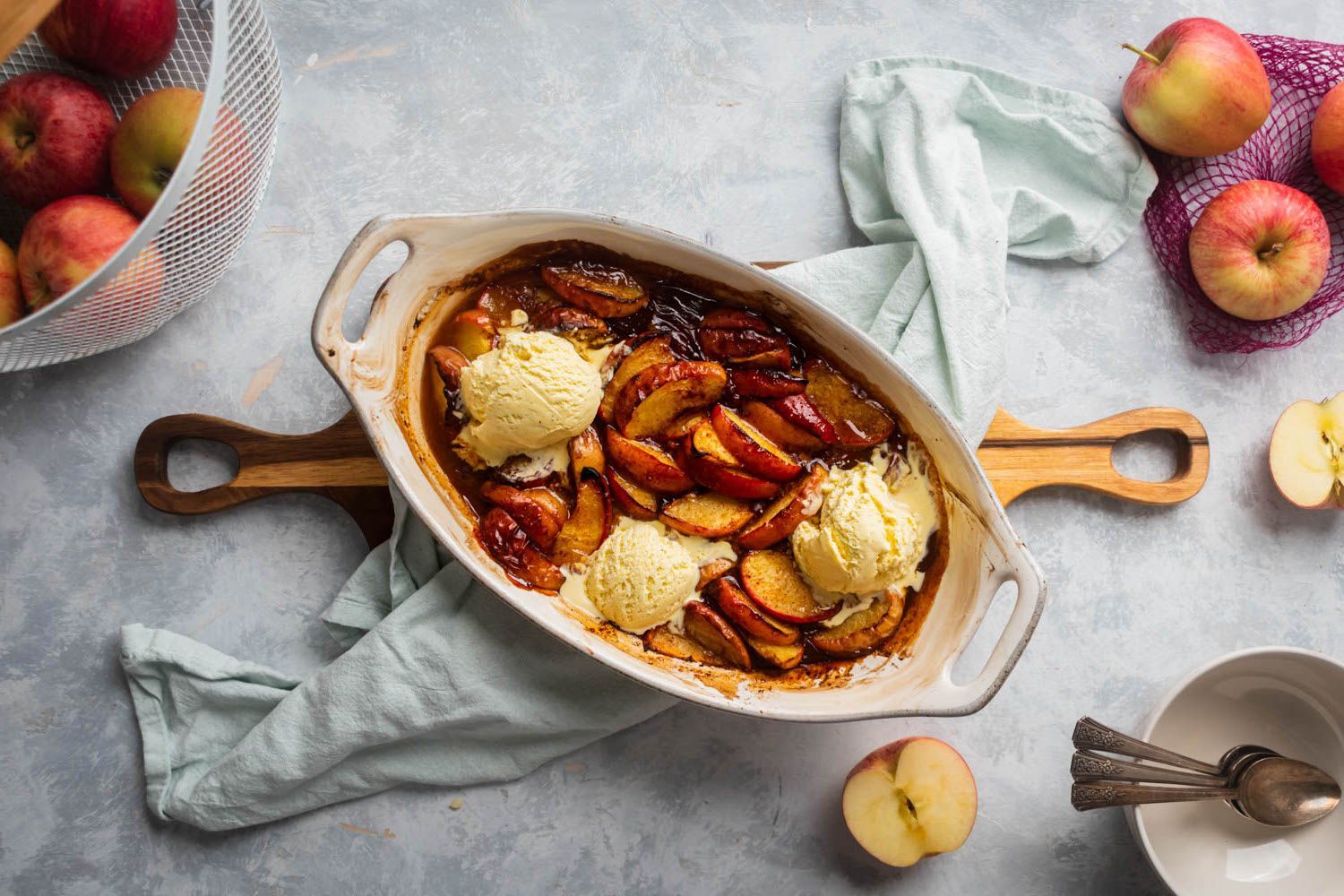 Baked apples in a ceramic baking dish with vanilla ice cream and cinnamon.