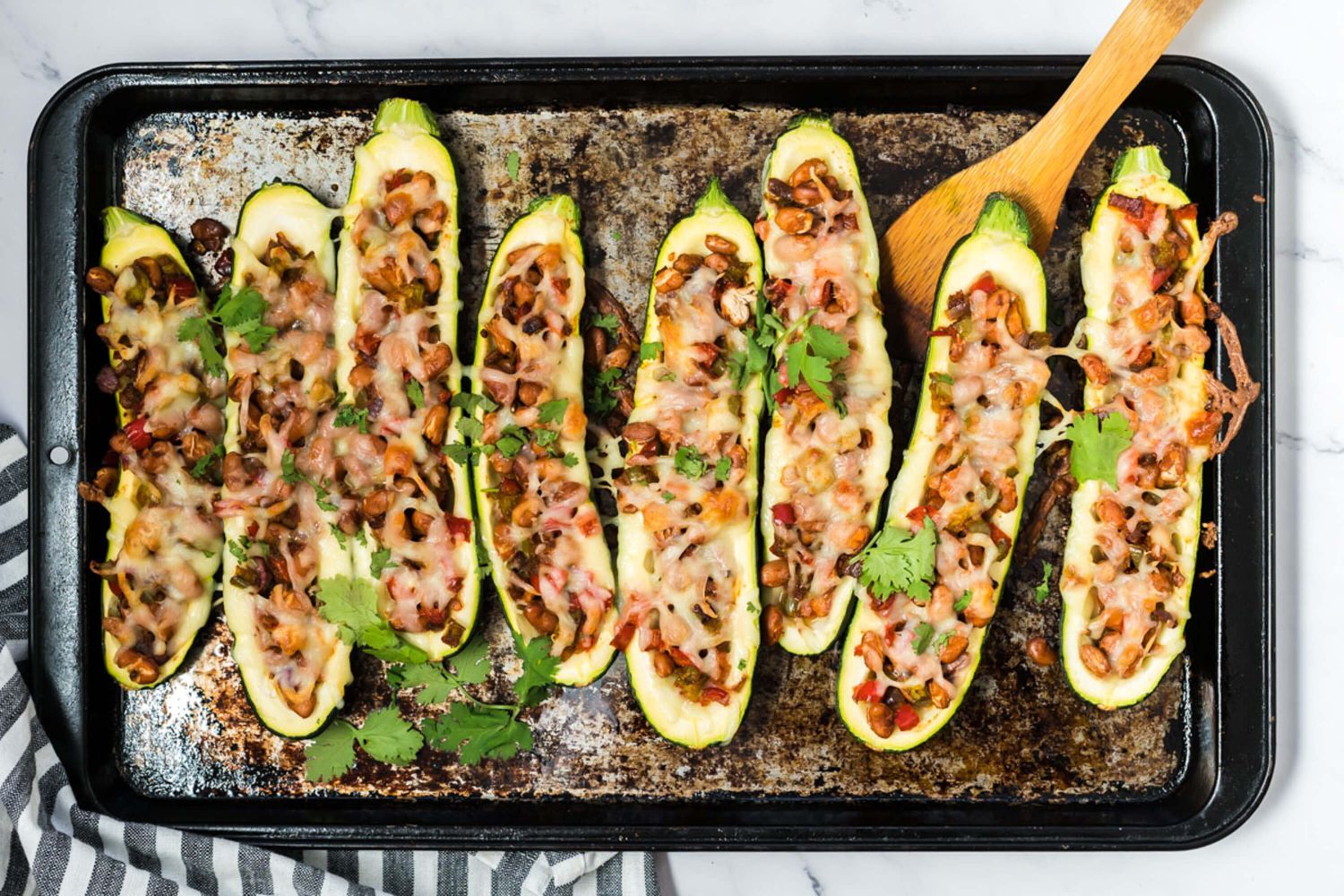 Fajita stuffed zucchini with pinto beans on a baking sheet with beans, peppers, onions, and melted cheese.