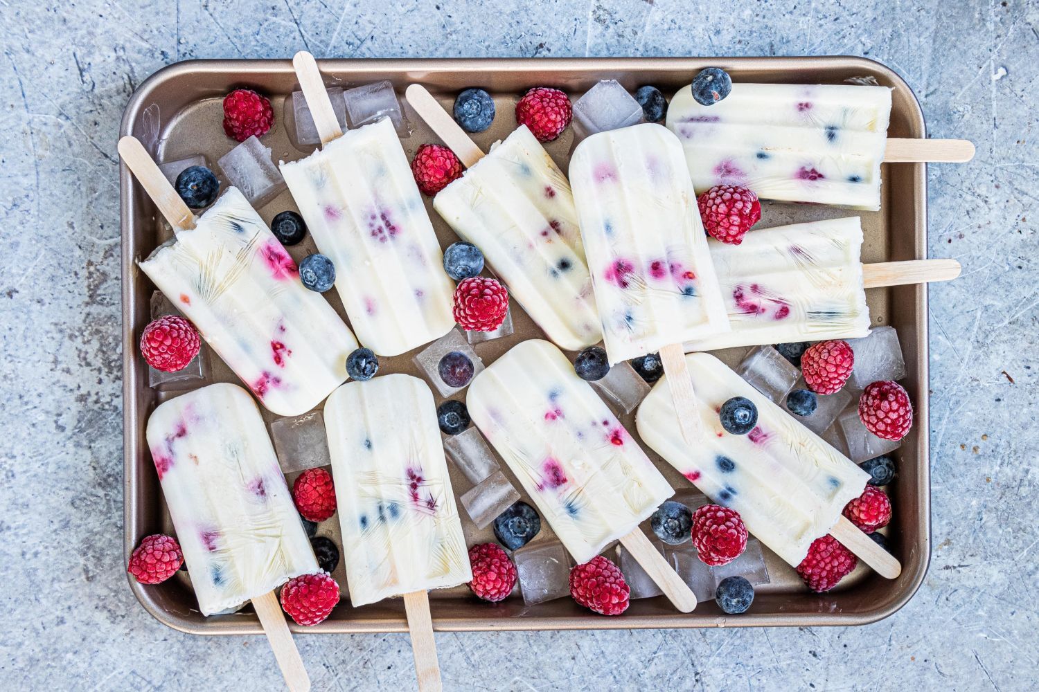Fruit and yogurt popsicles with blueberries and raspberries on a tray with ice.