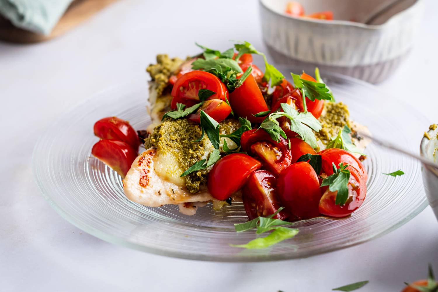 Grilled chicken margherita with cherry tomatoes, melted mozzarella cheese, and pesto on a plate.