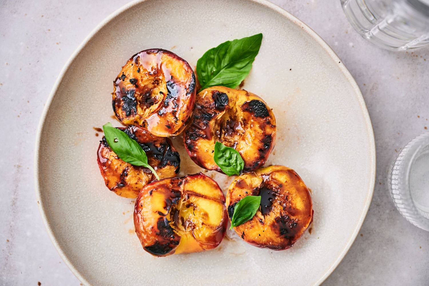 Grilled peaches with dark brown grill marks served on a plate with honey and fresh basil.