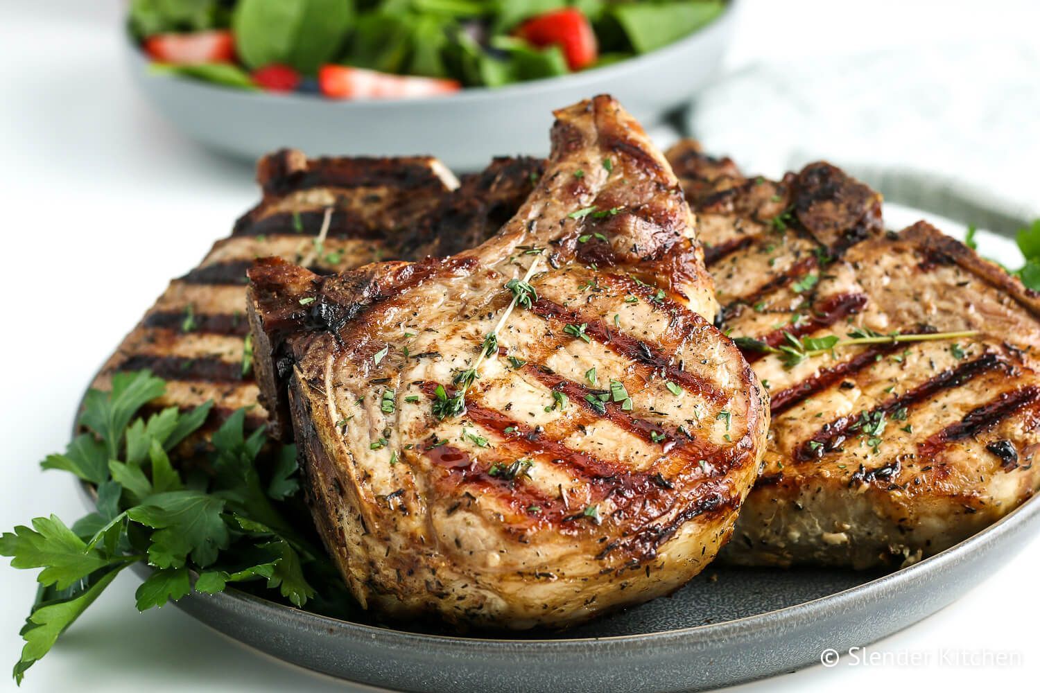 Grilled pork chops with grill marks and fresh thyme on a plate.