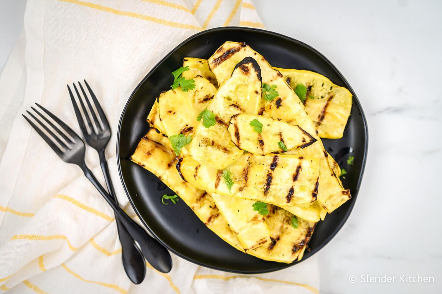 Grilled yellow squash on a black plate sprinkled with parsley.