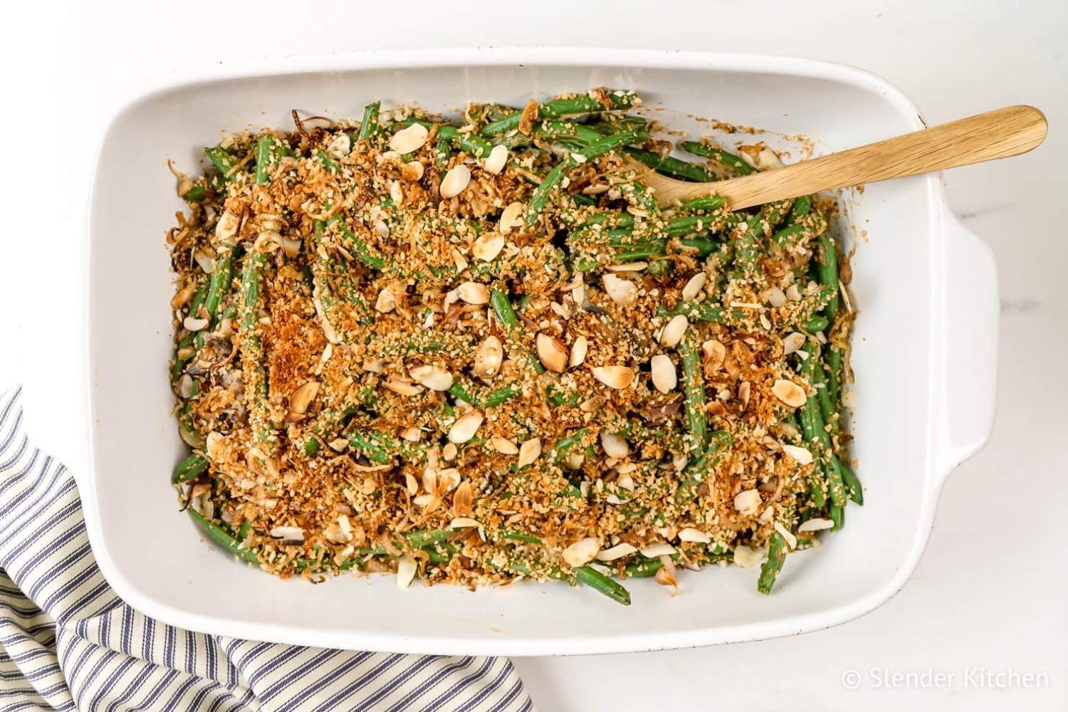 Healthy Green Bean Casserole with green beans, mushroom sauce, and a crispy almond onion topping in a baking dish with a striped napkin.