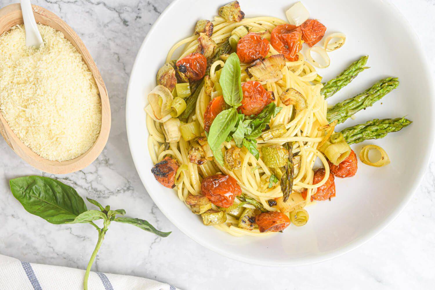 Healthy roasted vegetable pasta with tomatoes, asparagus, and onions with Parmesan and basil on the side.