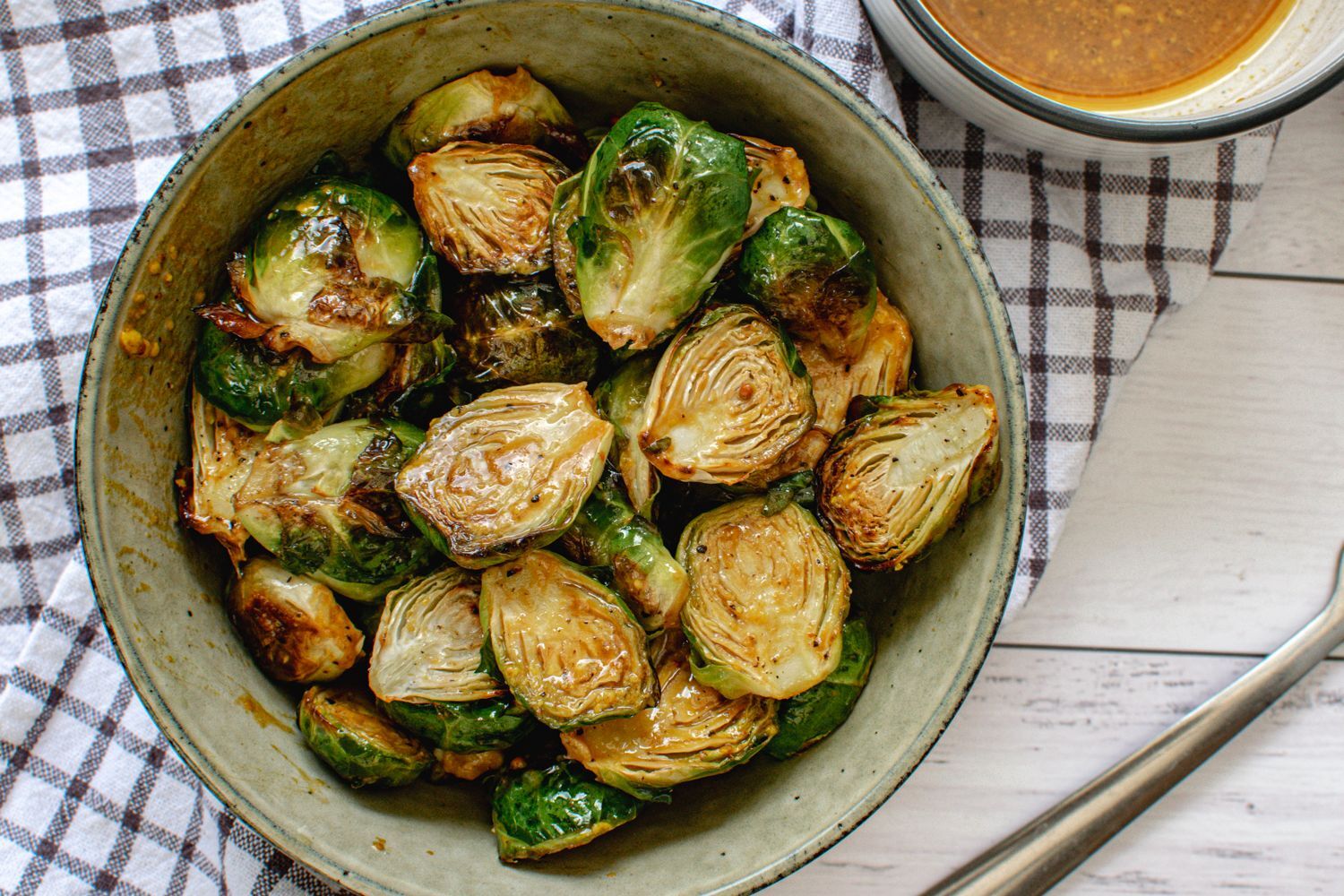 Honey mustard Brussels sprouts in a bowl with the sauce in a small bowl on the side.