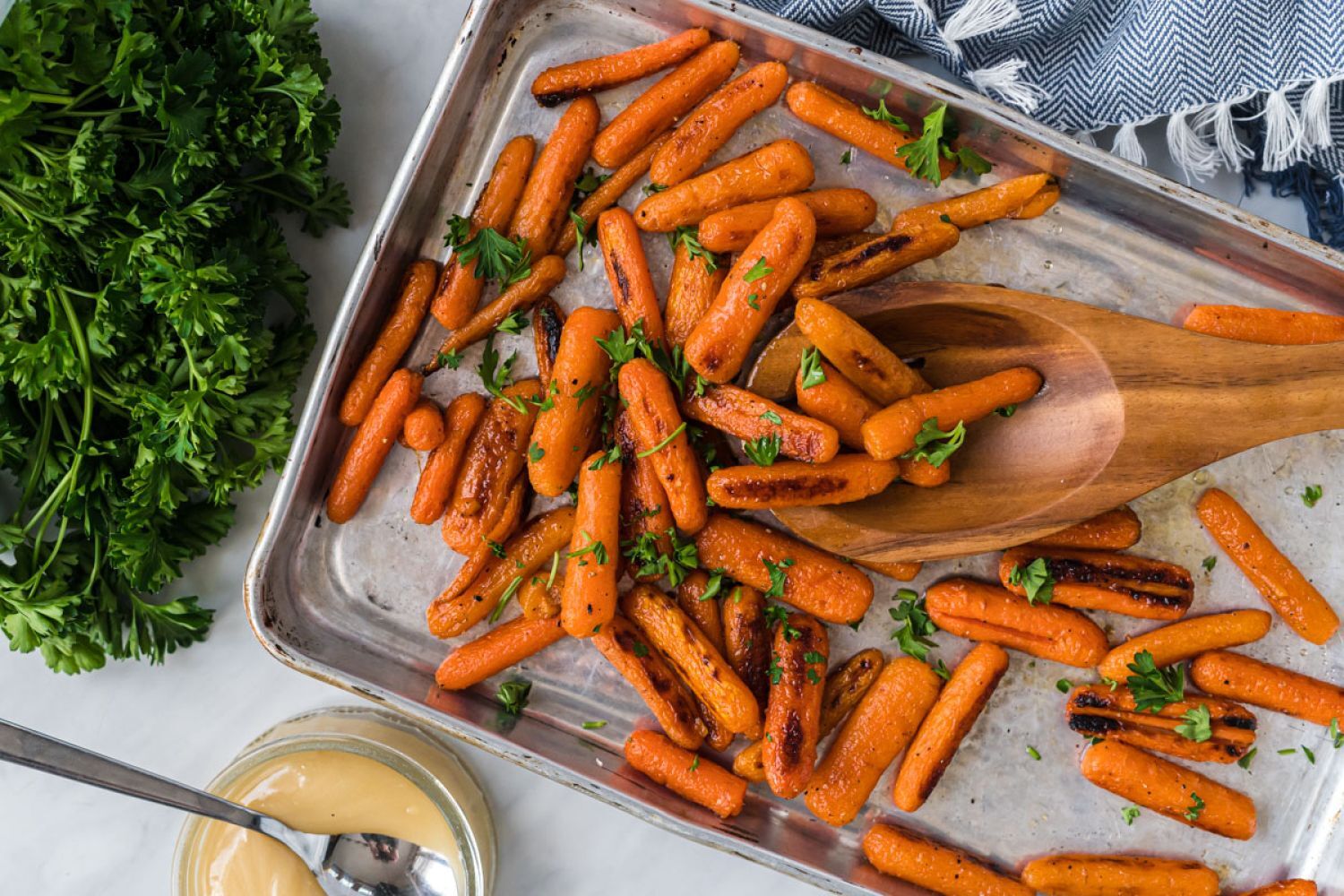 Honey roasted baby carrots with crispy edges on a baking sheet with salt, pepper, honey, and chopped parsley.