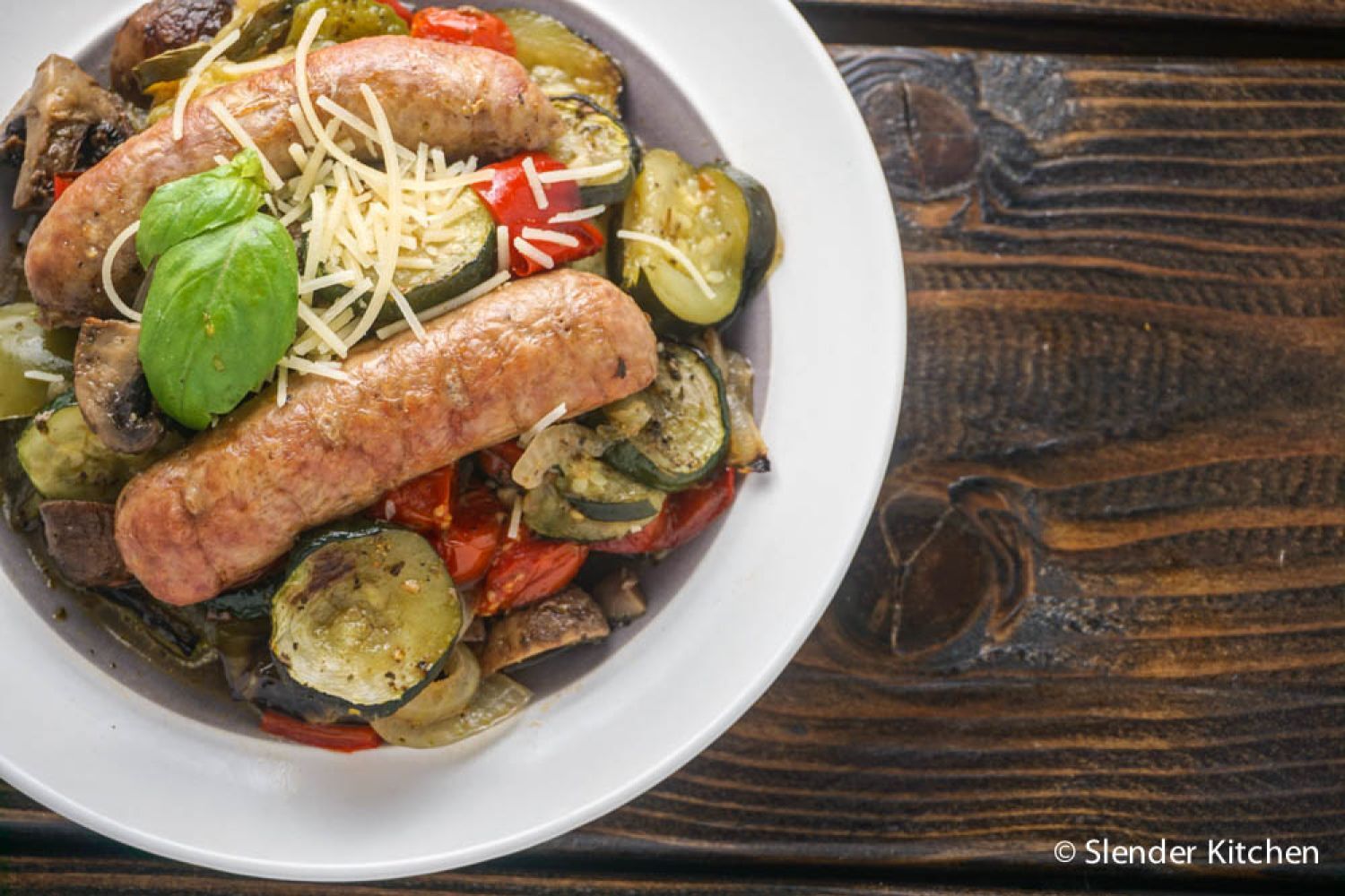 Italian sausages with tomatoes, zucchini, onions, and peppers in a bowl.
