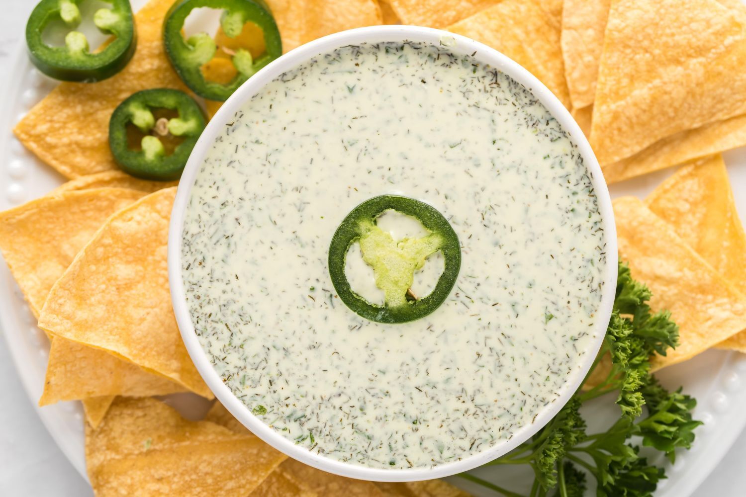 Jalapeno ranch dressing with Greek yogurt, herbs and jalapenos in a small dish with chips on the side.