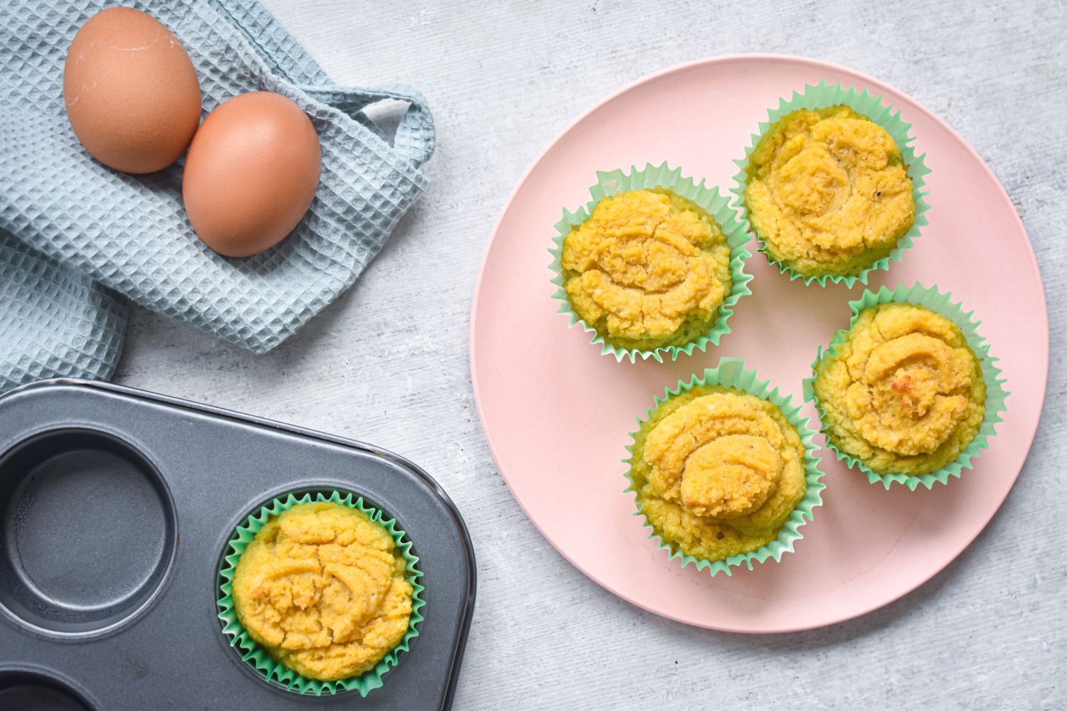 Low carb coconut muffins made with coconut flour on a pink plate with a muffin tin on the side.