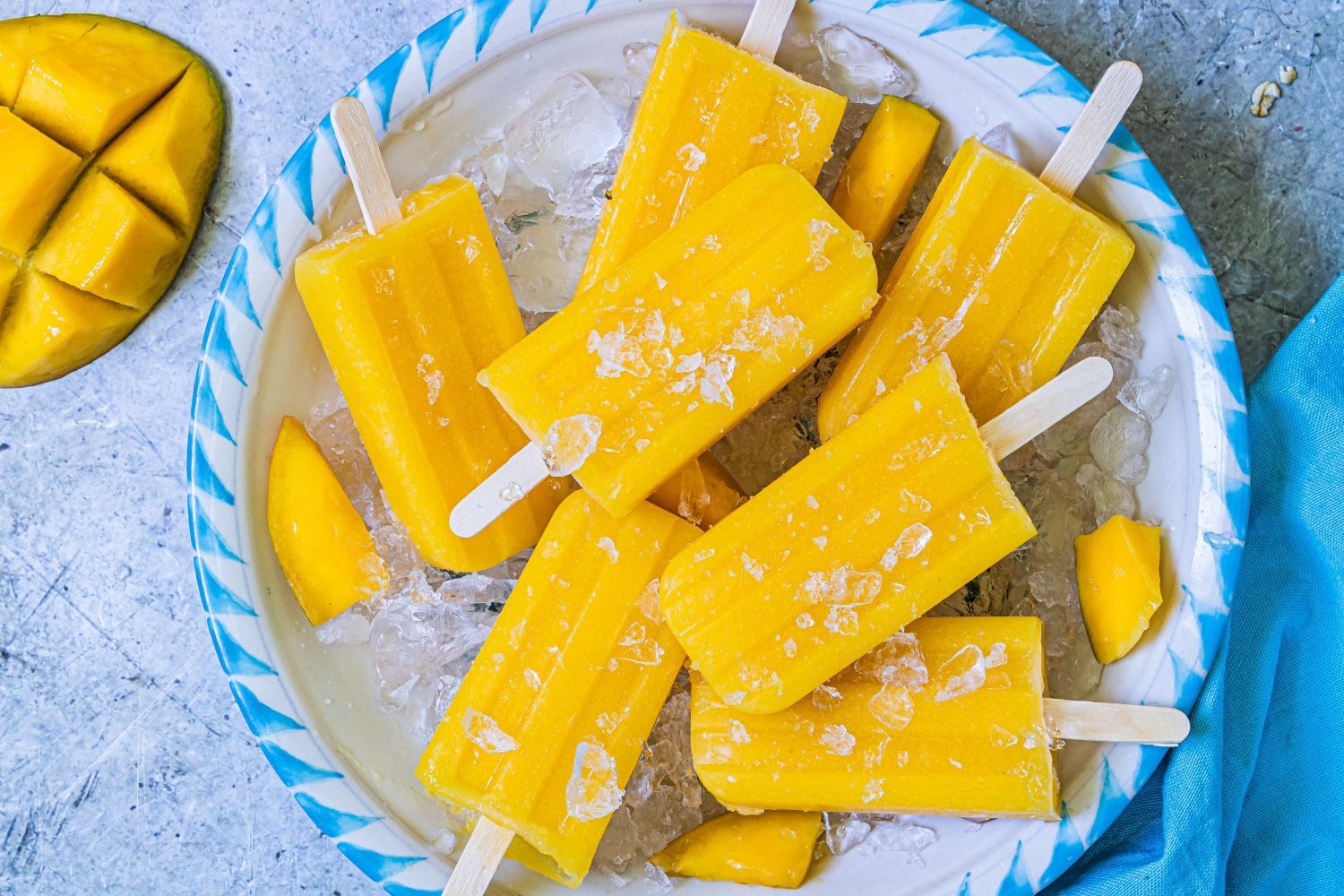Mango popiscles made with fresh mango pieces, lime juice, water, and honey on a plate with ice.