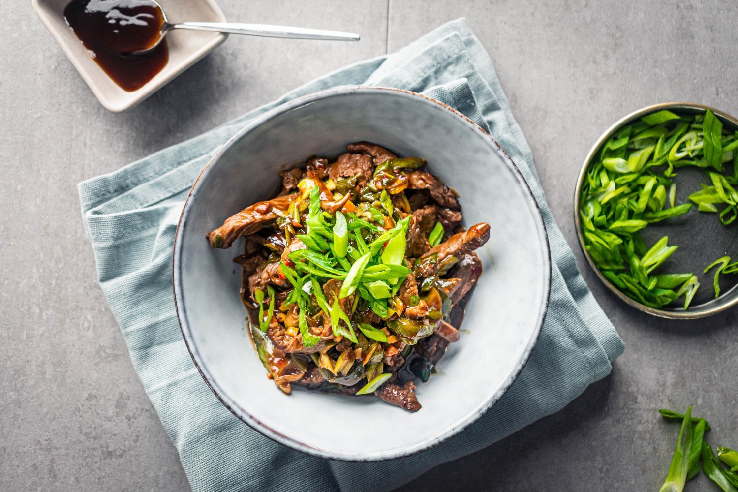 Healthy Mongolian Beef in a bowl with chopsticks with scallions and sesame seeds.