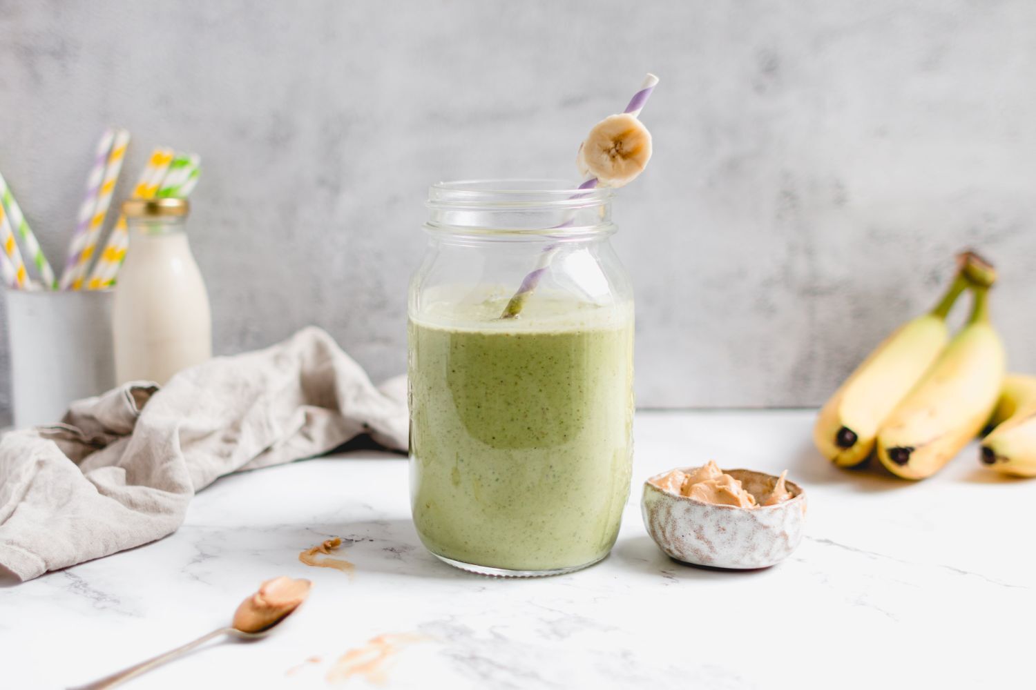 Peanut butter banana green smoothie served in a glass with a slice of banana and a straw.