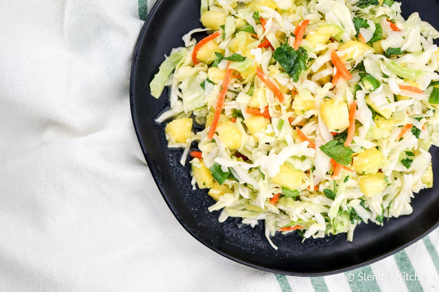 Pineapple coleslaw with carrots, pineapple, cabbage, cilantro, and coconut dressing in a bowl.