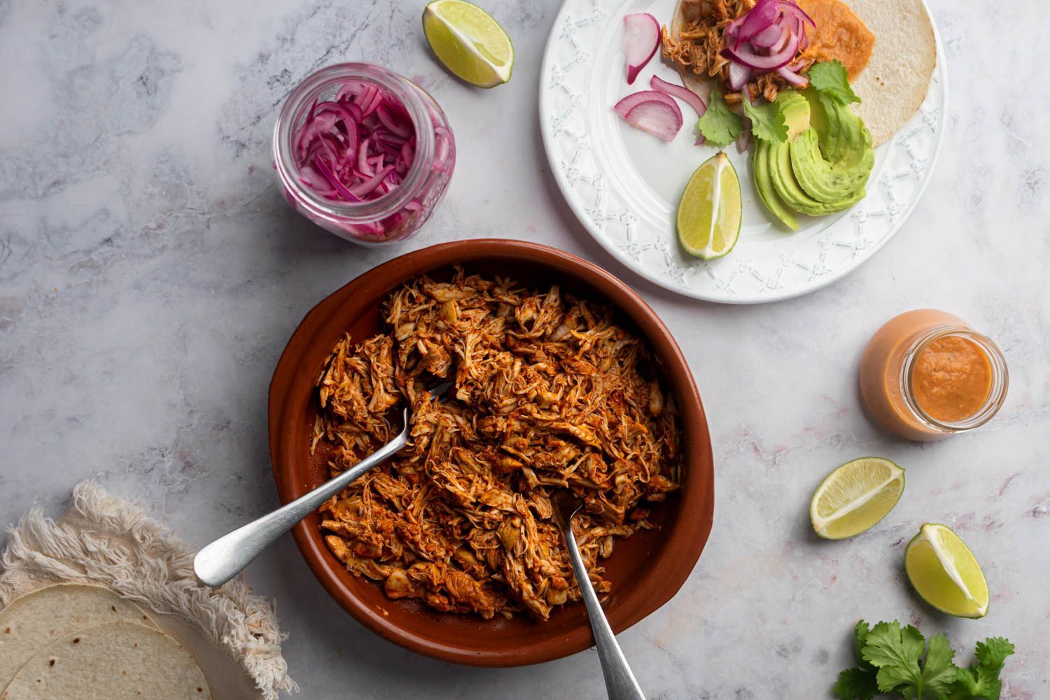 Mexican pollo pibil shredded in a bowl and served in a corn tortilla with pickled onions and habanero salsa.