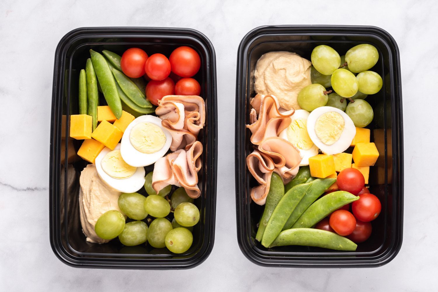 Copycat Starbucks Protein Snack Box in two containers with hard boiled eggs, hummus, vegetables, fruit, and deli turkey.