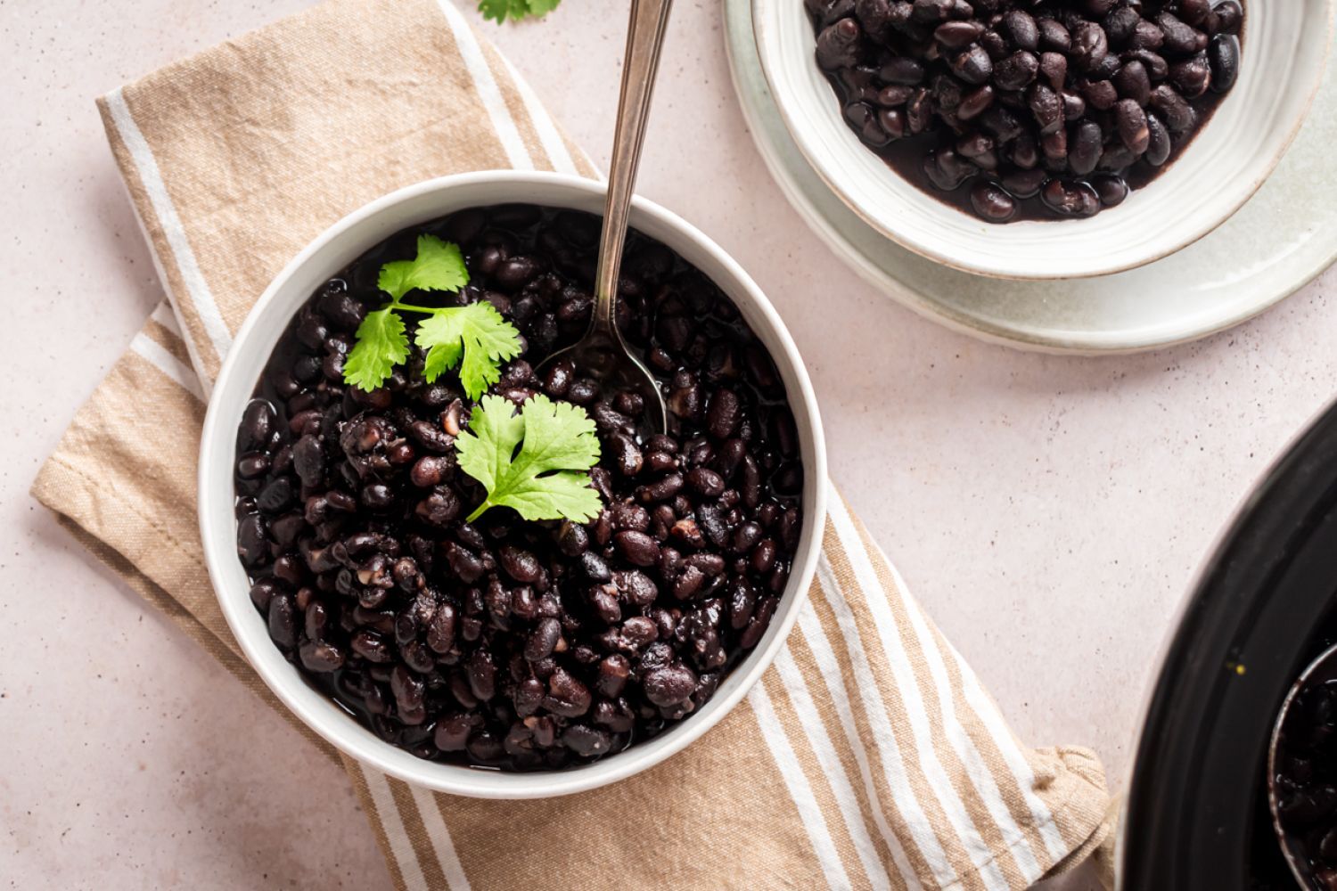 Slow cooker black beans served in two bowls with cilantro and a spoon.