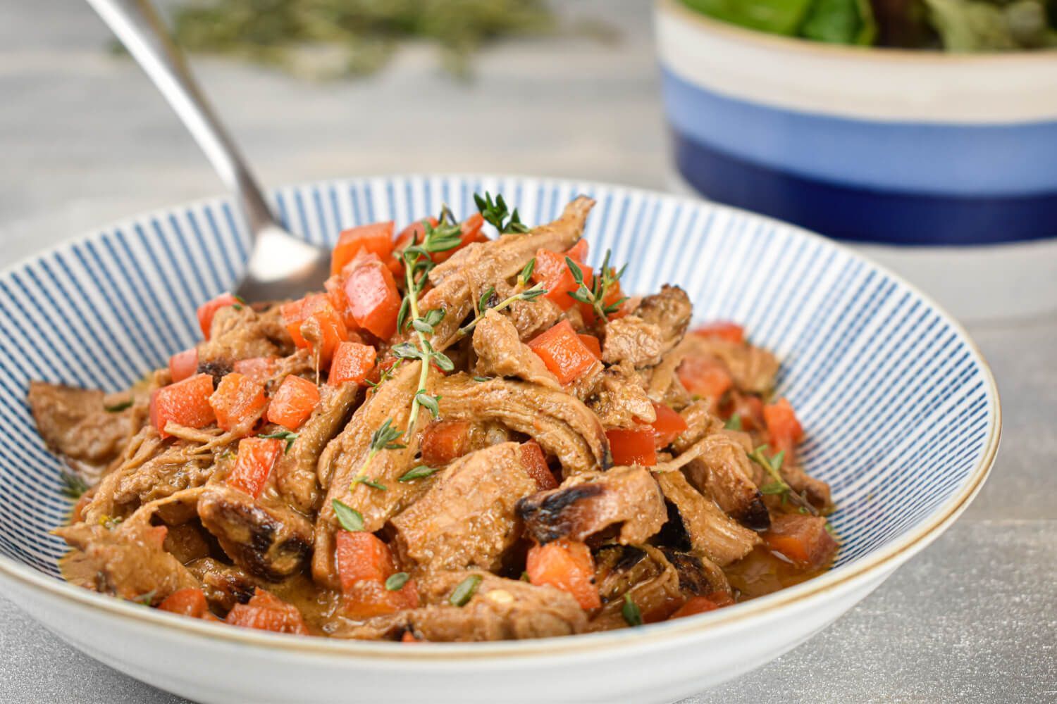 Slow cooker pork paprikash in a bowl with tomatoes and sour cream in a bowl.