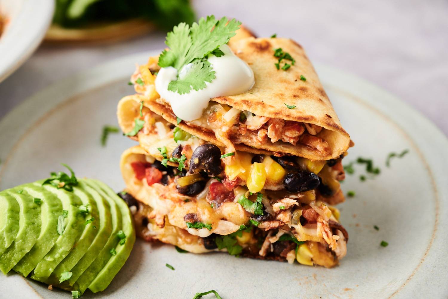 Spicy chicken quesadillas with shredded chicken, melted cheese, black beans, and corn in flour tortillas with sour cream, avocado, and cilantro.