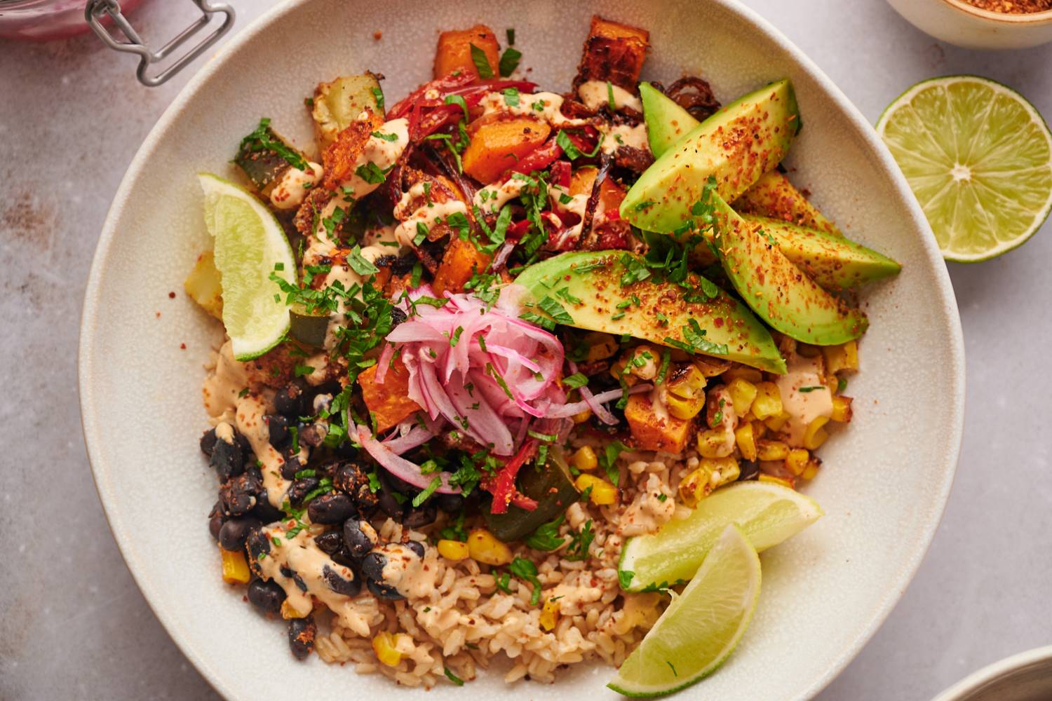 Sweet potato bowls with roasted sweet potatoes, black beans, corn, peppers, onions, zucchini, and brown rice topped with avocado, cilantro, and limes.