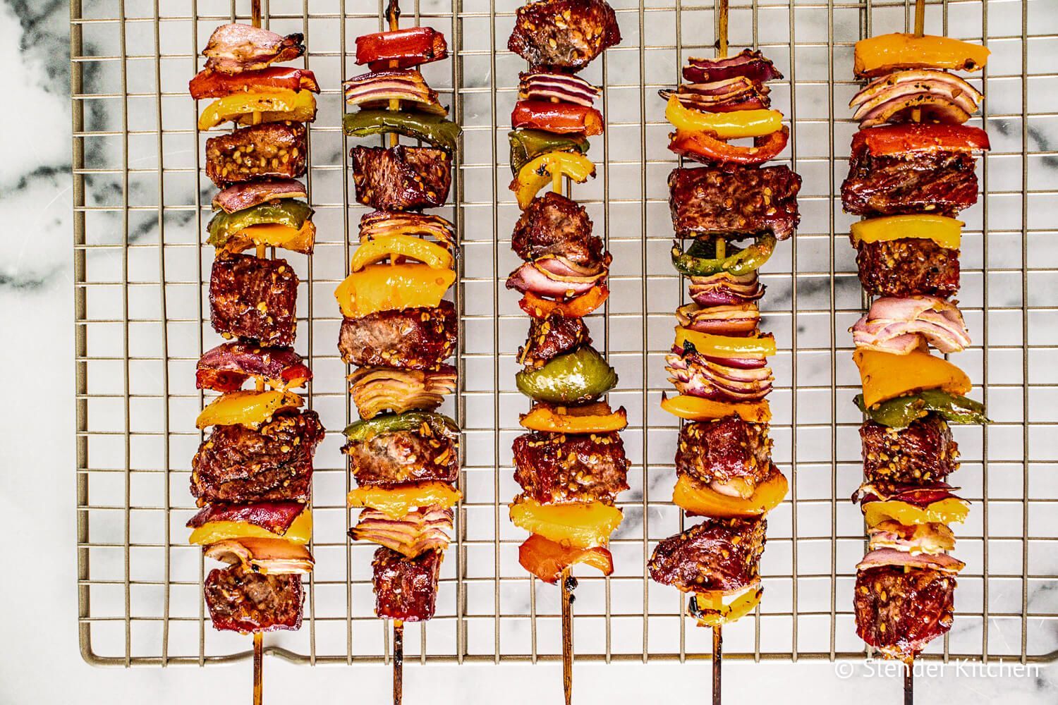 Teriyaki beef kabobs with red onions, bell peppers, and teriyaki sauce on skewers on a rack. 