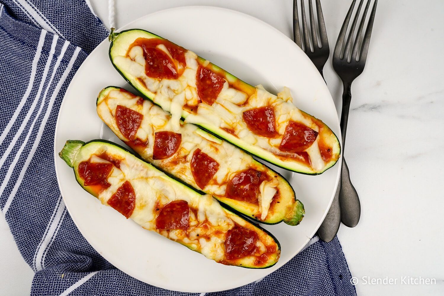 Zucchini pizza boats with marinara sauce, melted mozzarella cheese, and pepperoni on a white plate.